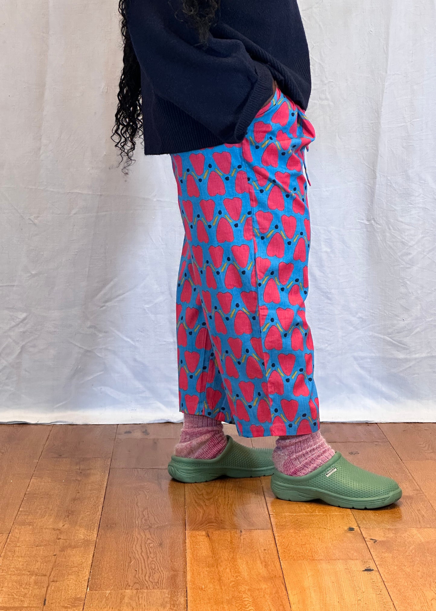 Person wearing blue pants with red heart patterns and green shoes on a wooden floor. Humphries and Begg