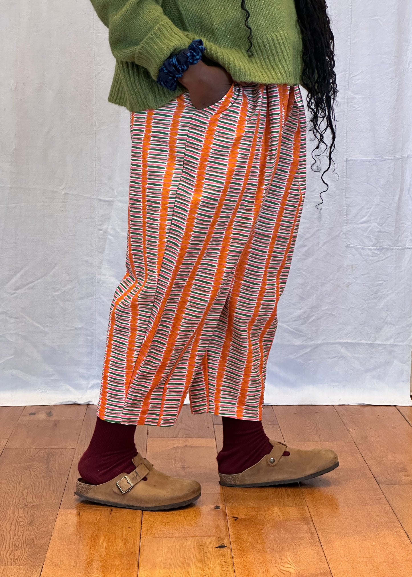 Person wearing a green sweater and orange striped pants on a wooden floor. Humphries and Begg