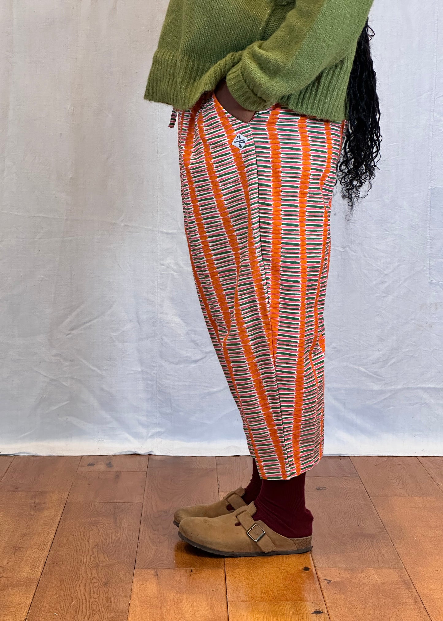 Person wearing a green sweater and patterned pants walking on a wooden flooring. Humphries and Begg