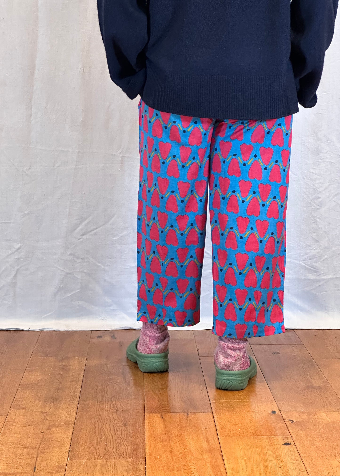 Person wearing a navy sweater and patterned trousers on a wooden floor.