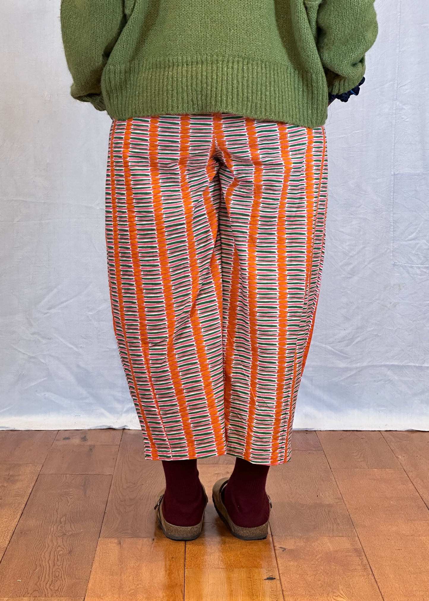Person wearing a green sweater and orange striped trousers on a wooden floor. Humphries and Begg