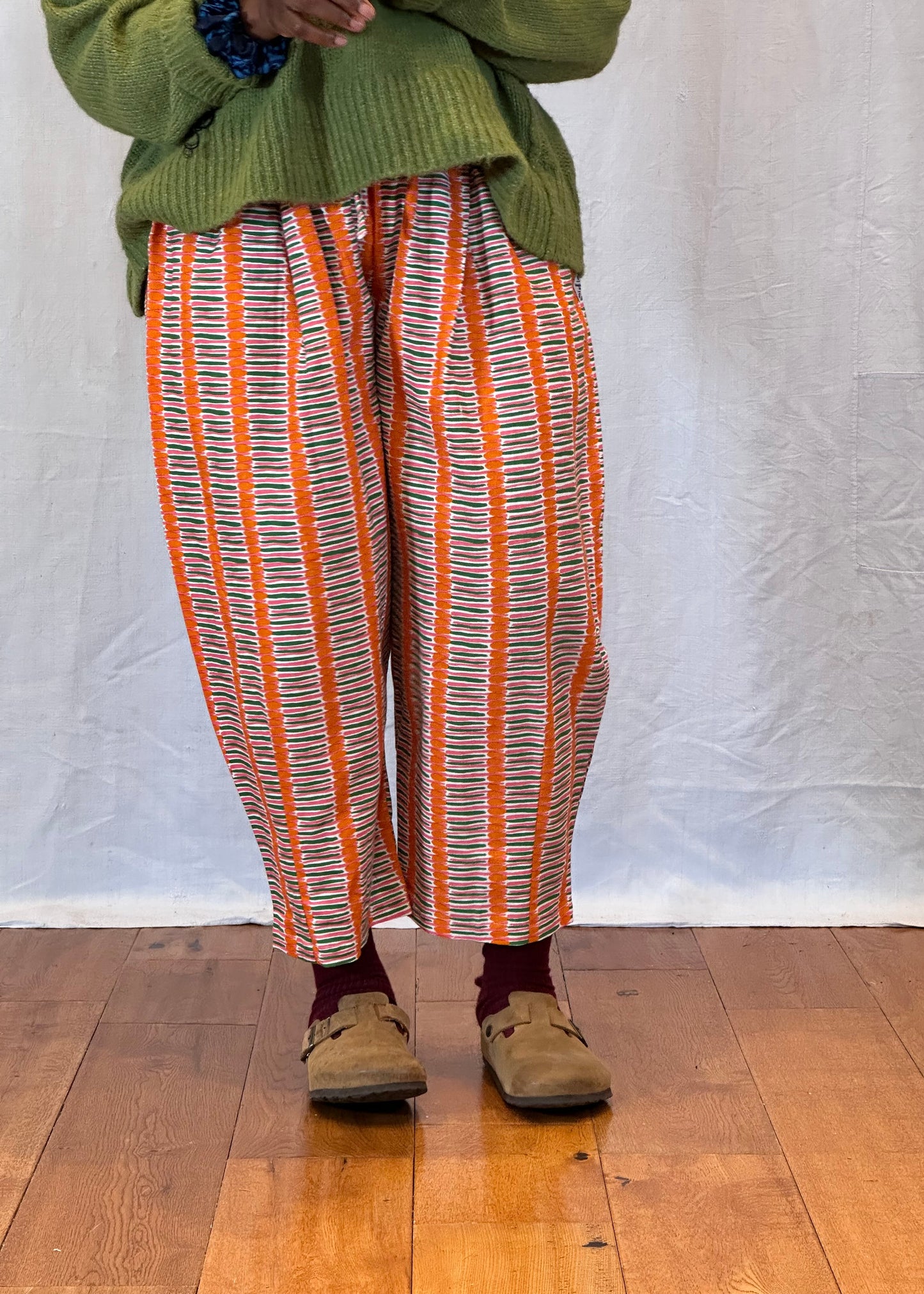 Person wearing a green sweater and striped trouser on a wooden floor. Humphries and Begg