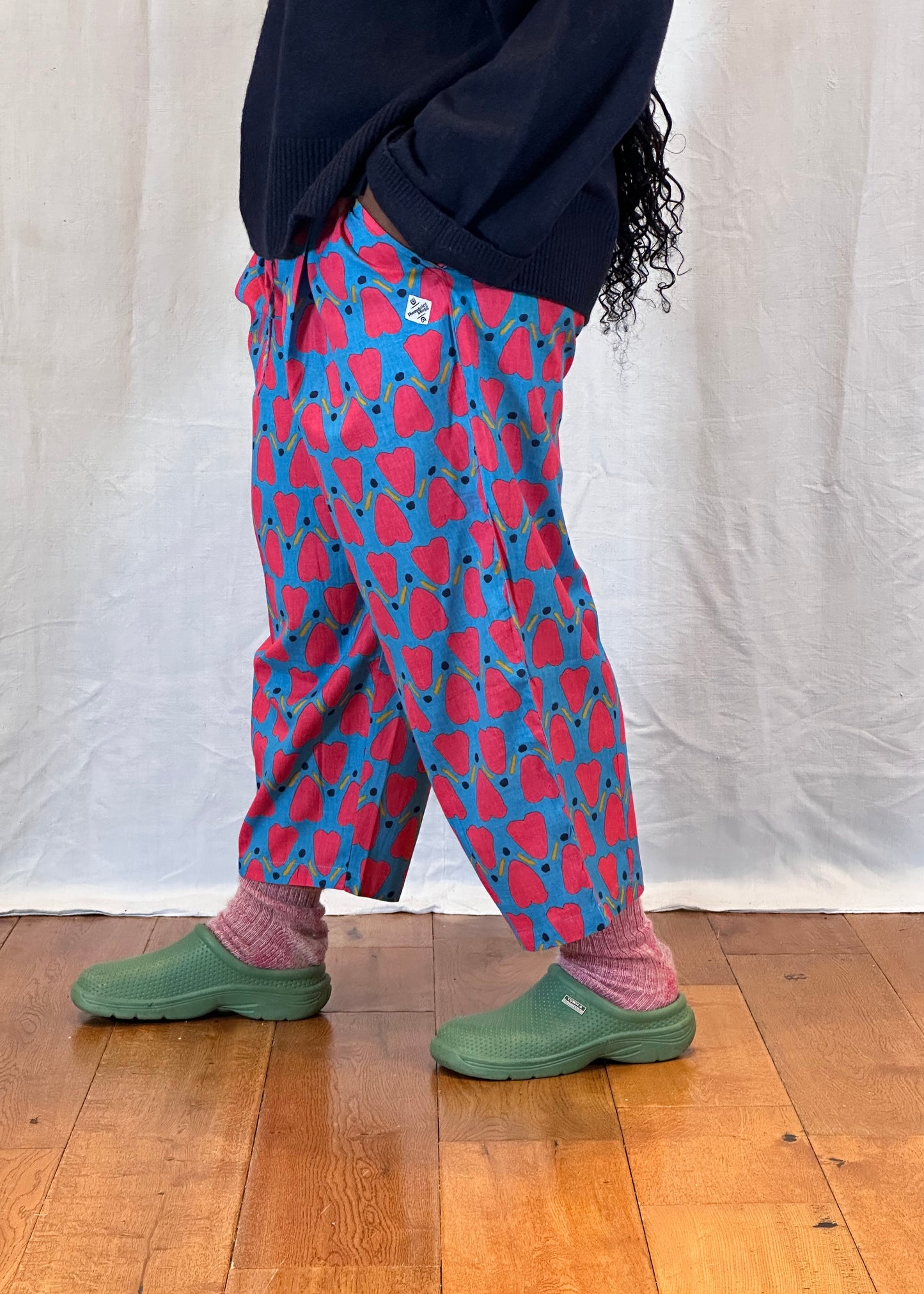 Person wearing a blue and red patterned trousers with green shoes on a wooden floor.