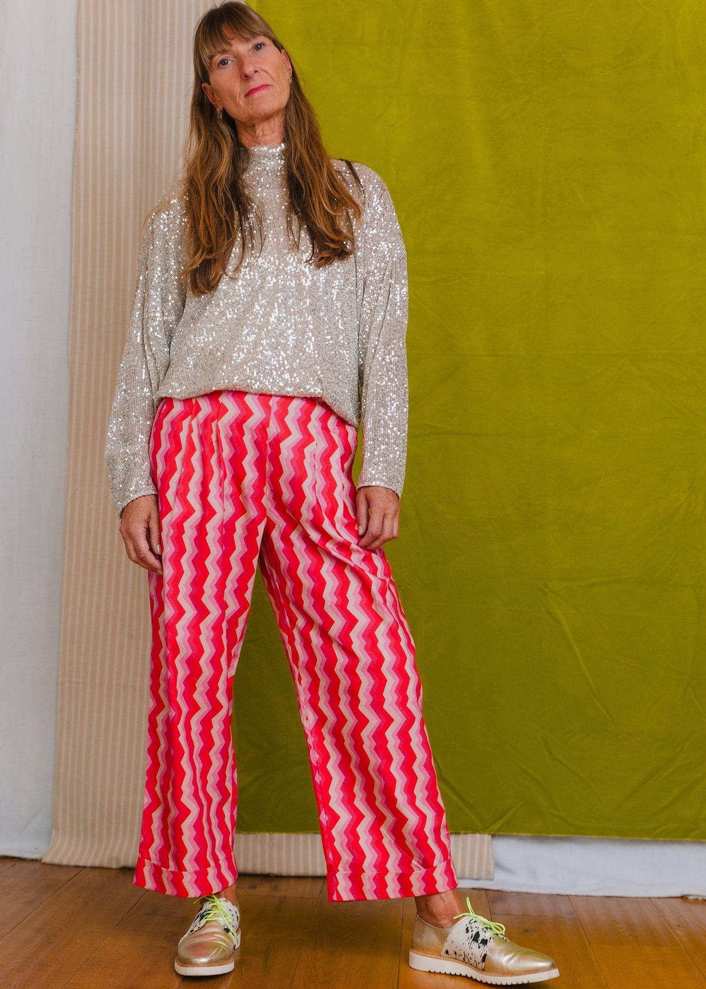 Woman wearing a sequined top and red and white striped pants against a green wall.