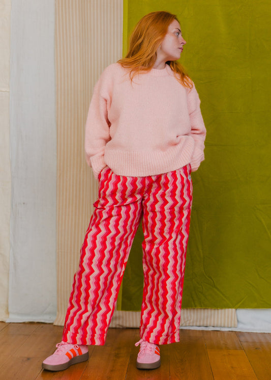 Person wearing a pink sweater and red striped pants standing against a green wall.