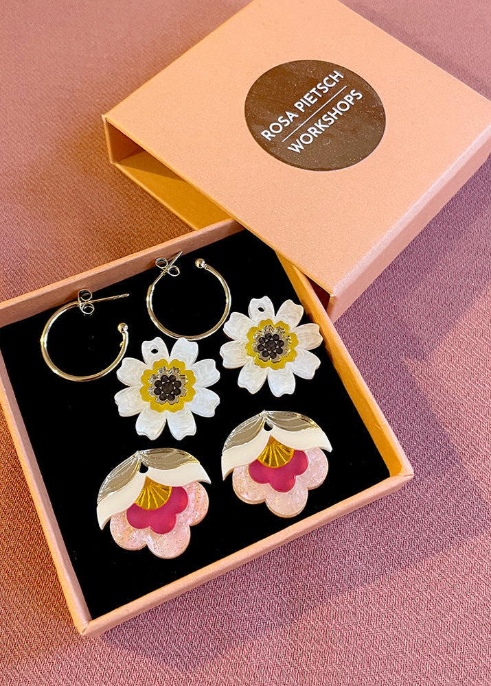 Floral earrings in a box with 'Rosa Pietzch Workshops' branding on a pink background