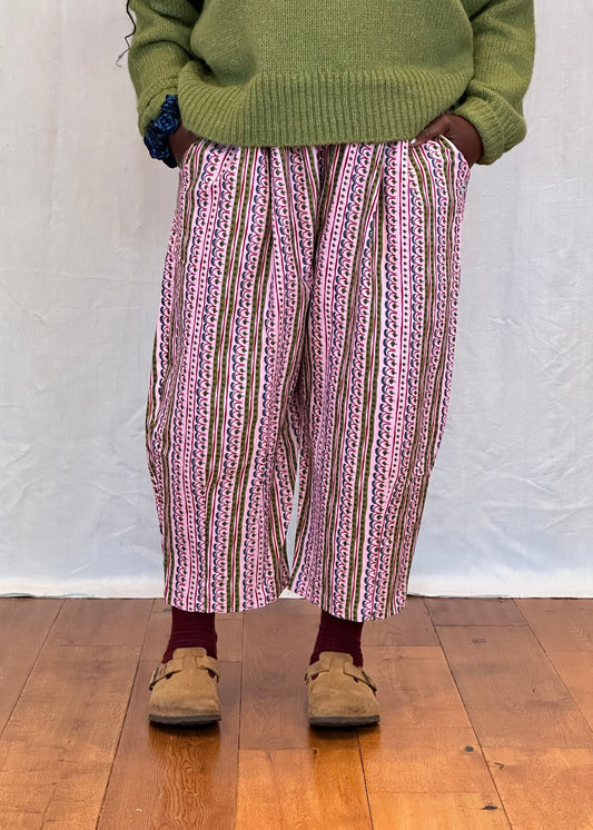 Person wearing a green sweater and patterned trousers standing on a wooden floor.