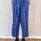 Person wearing blue patterned pants standing on a white sheet with a wooden floor.