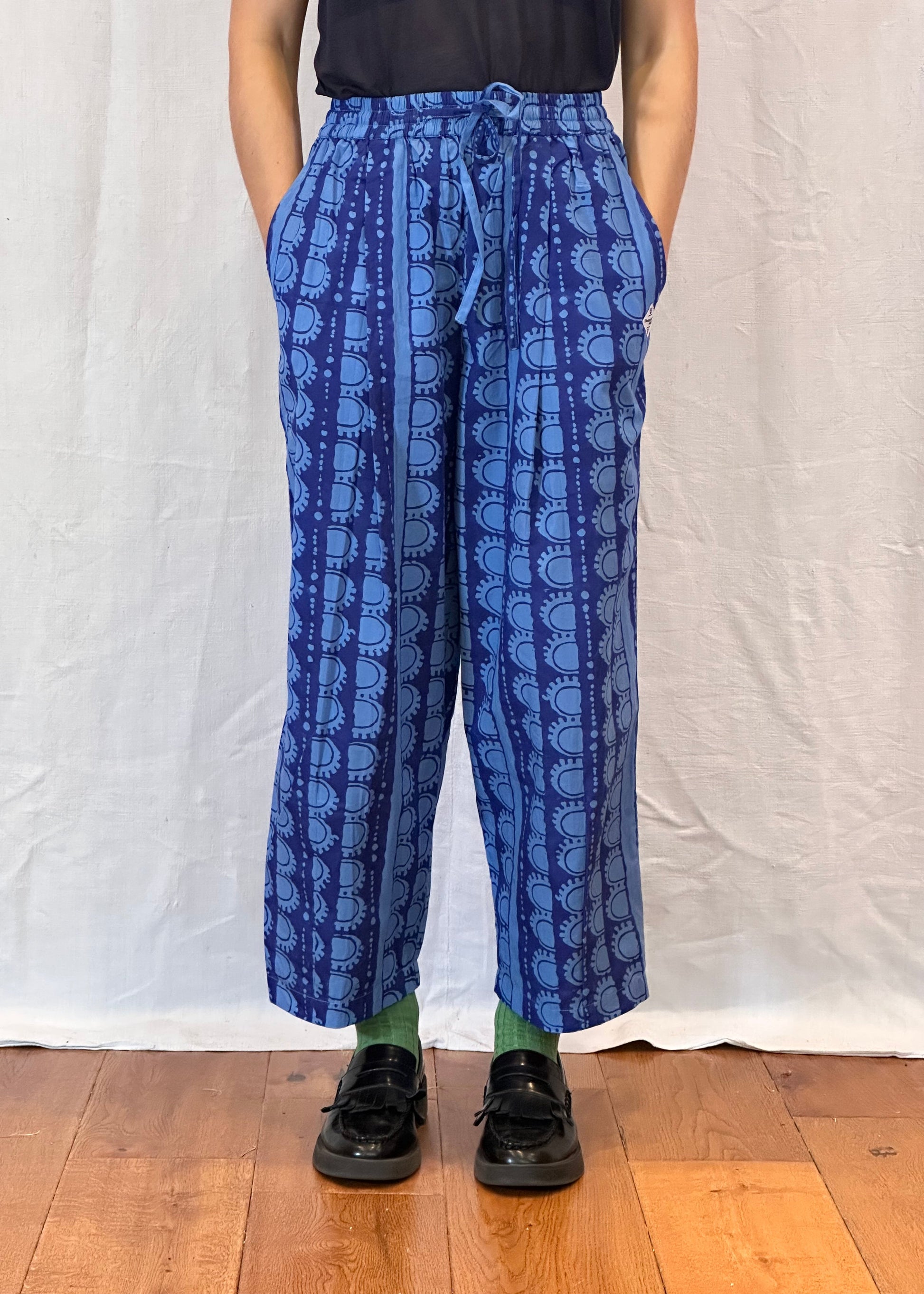 Person wearing blue patterned pants standing on a white sheet with a wooden floor.