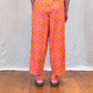 Person wearing bright pink and orange patterned pants on a wooden floor.