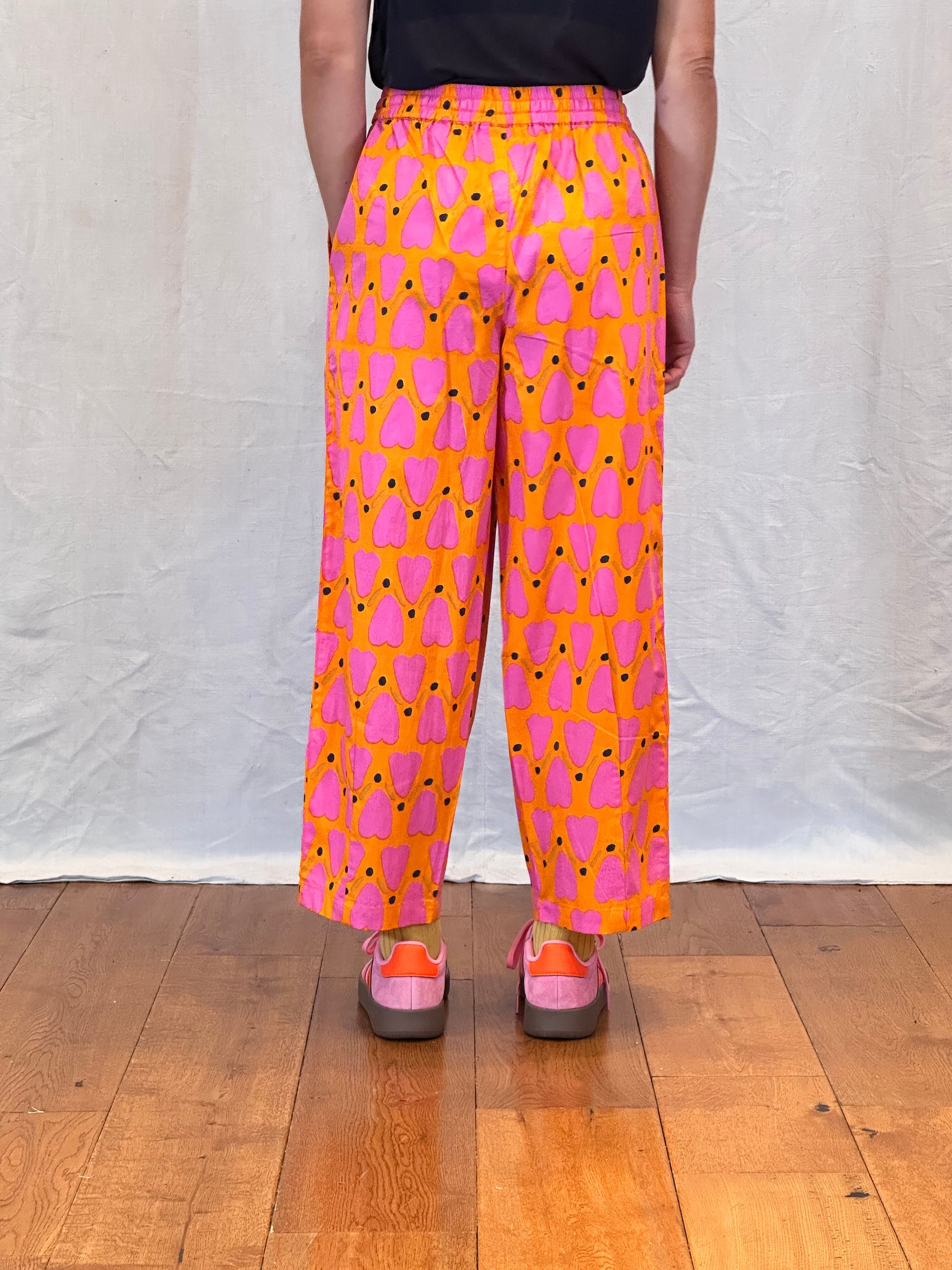 Person wearing bright pink and orange patterned pants on a wooden floor.
