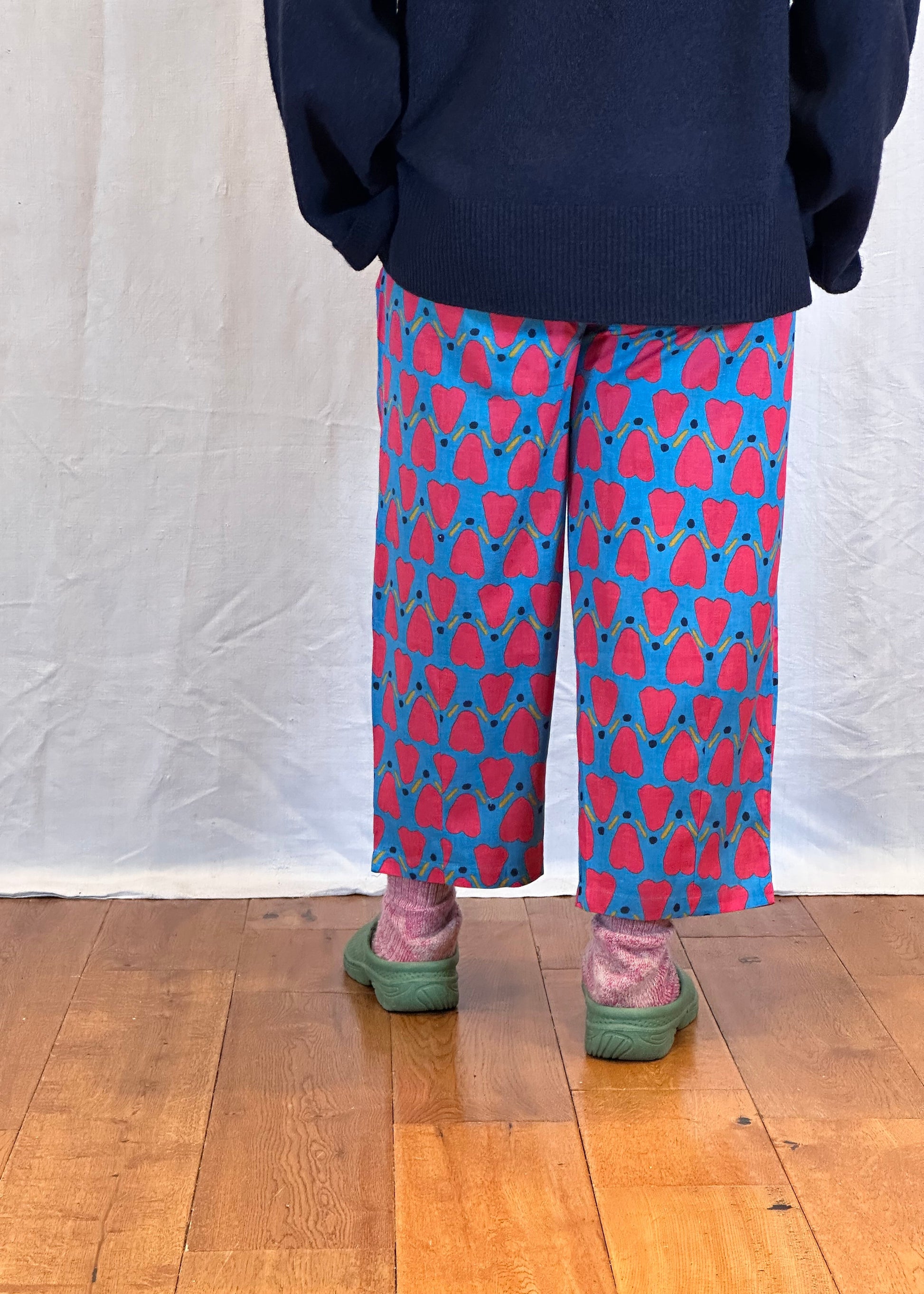 Person wearing a navy sweater and patterned trousers on a wooden floor.