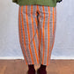 Person wearing a green sweater and orange striped trousers on a wooden floor. Humphries and Begg