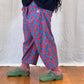 Person wearing a blue and red patterned trousers with green shoes on a wooden floor.