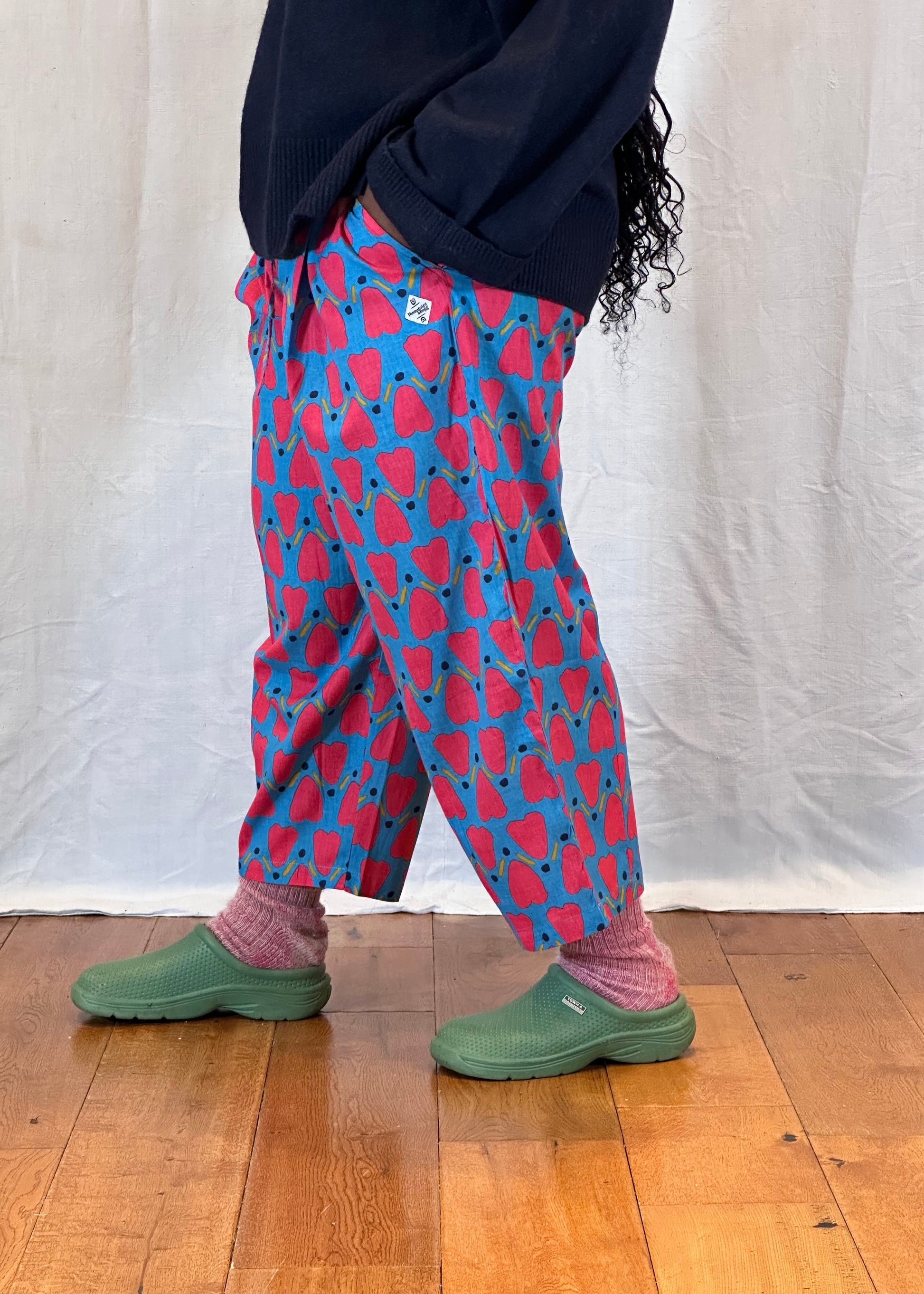 Person wearing a blue and red patterned trousers with green shoes on a wooden floor.
