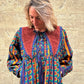 Woman wearing a colorful patterned dress against a stone wall.