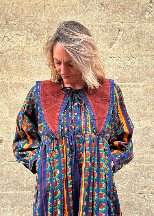 Woman wearing a colorful patterned dress against a stone wall.