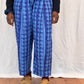 Person wearing blue patterned trousers on a white backdrop with wooden floor.