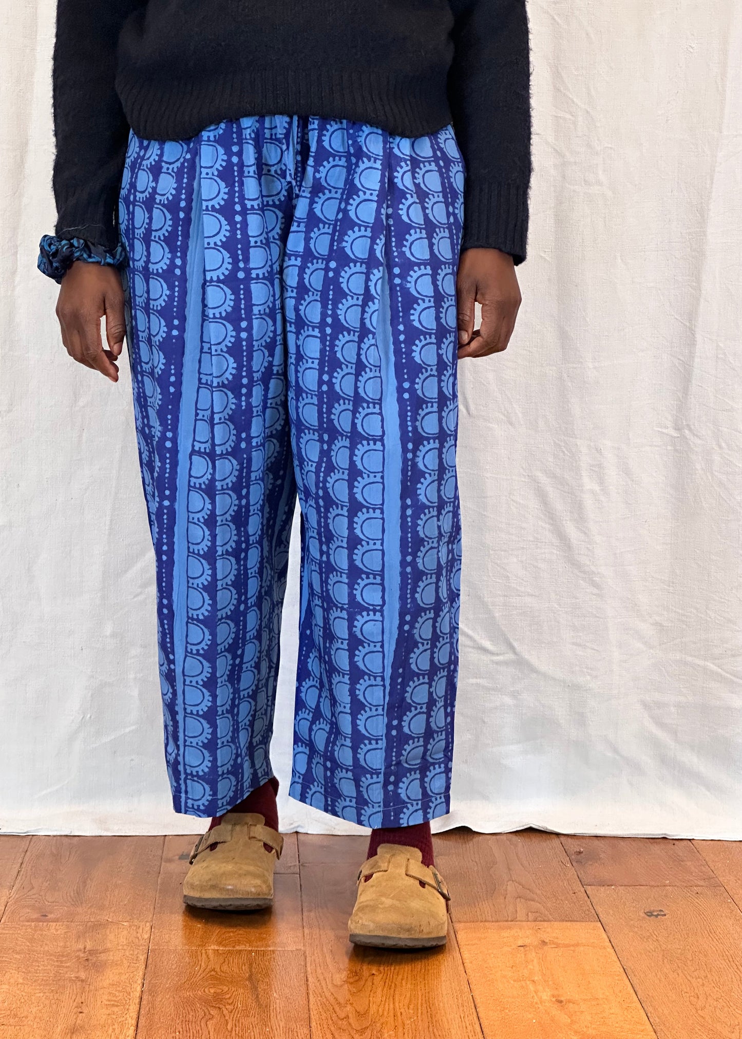 Person wearing blue patterned trousers on a white backdrop with wooden floor.