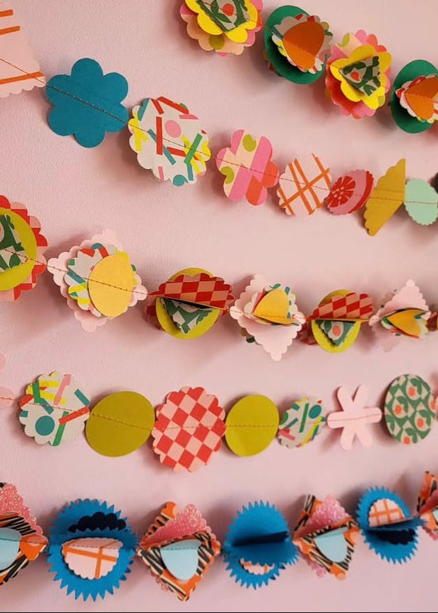 Colorful paper garland with various shapes on a pink background
