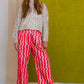 Woman wearing a sequined top and red and white striped pants against a green wall.