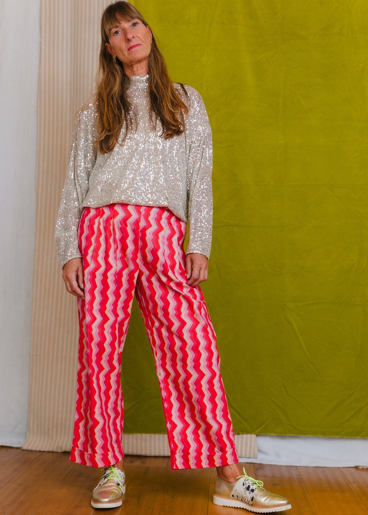 Woman wearing a sequined top and red and white striped pants against a green wall.