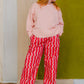Person wearing a pink sweater and red striped pants standing against a green wall.