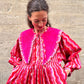 Woman wearing a pink and red patterned dress against a stone wall with long pointy collar.