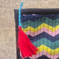 Colorful zigzag patterned fabric with a red tassel on a textured surface