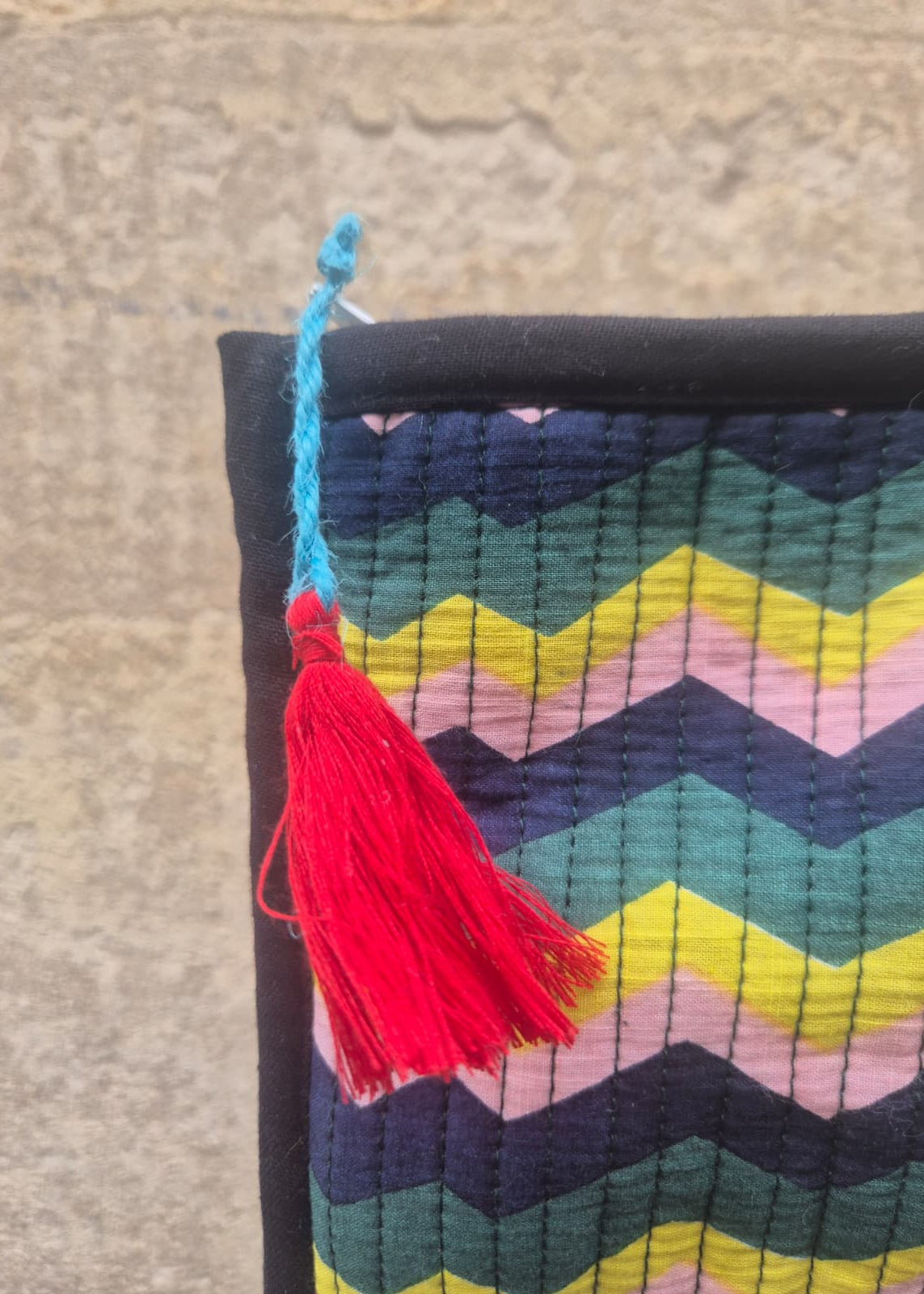 Colorful zigzag patterned fabric with a red tassel on a textured surface