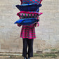 Person holding a stack of colorful pillows against a stone wall.
