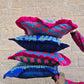 Stack of colorful patterned cushions against a stone wall.