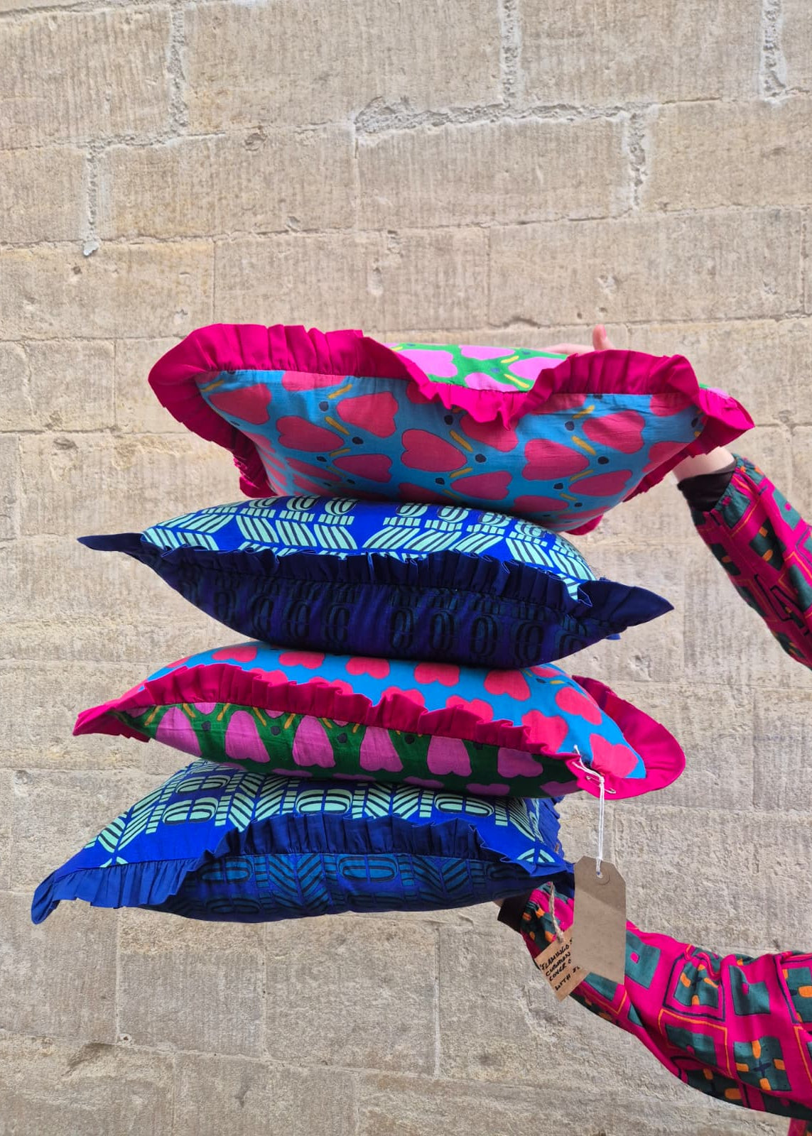 Stack of colorful patterned cushions against a stone wall.